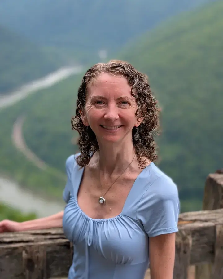 Jen smiling at a mountain overlook, resting a hand on a wooden railing